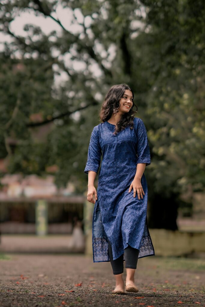 Woman in a blue kurti smiling and walking barefoot in a garden setting.