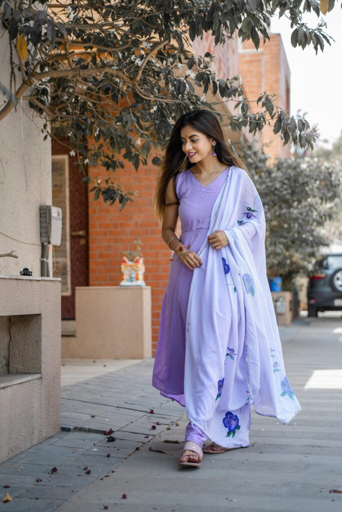 A smiling woman in a lilac dress walks outdoors while enjoying a sunny day.